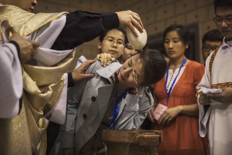 Image: Chinese Catholic Bishop Zhang Hong, left, pours holy water on the head of a worshipper during a special baptism ceremony on Holy Saturday