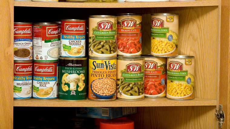 Wooden kitchen cupboard with shelves full of canned soup and vegetables