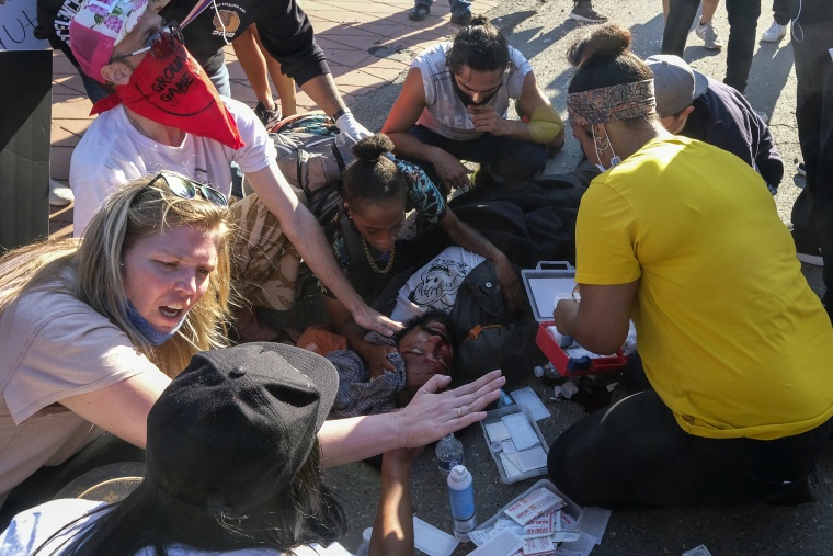 Demonstrators help a man who was sitting on a police car and injured by falling onto the ground during a protest to demand justice for George Floyd in downtown Los Angeles on May 27, 2020.