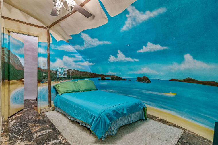Một phòng ngủ có họa tiết bãi biển nhiệt đới với bộ khăn trải giường màu xanh mòng két phù hợp. 